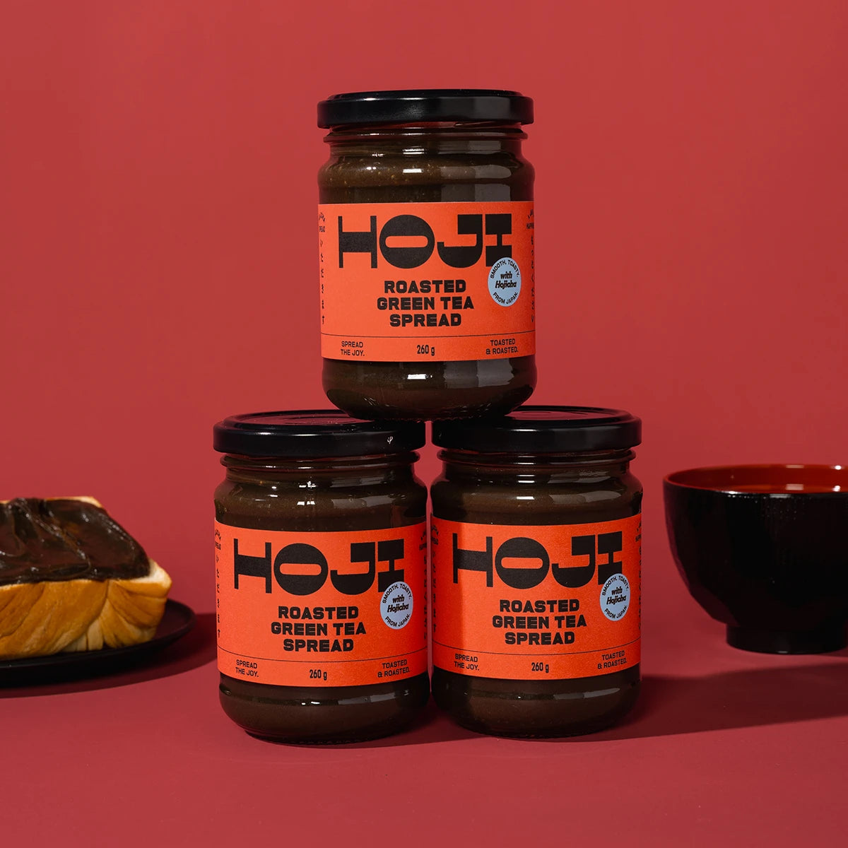 Three jars of HOJi roasted green tea spread on a red background