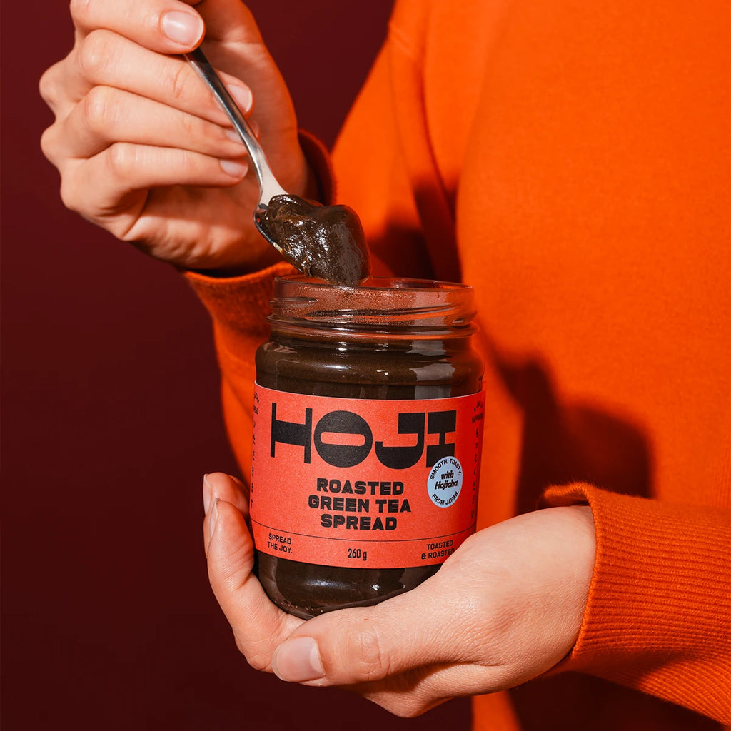 Person holding a jar of HOJI Roasted Green Tea Spread with a spoonful of spread above it.