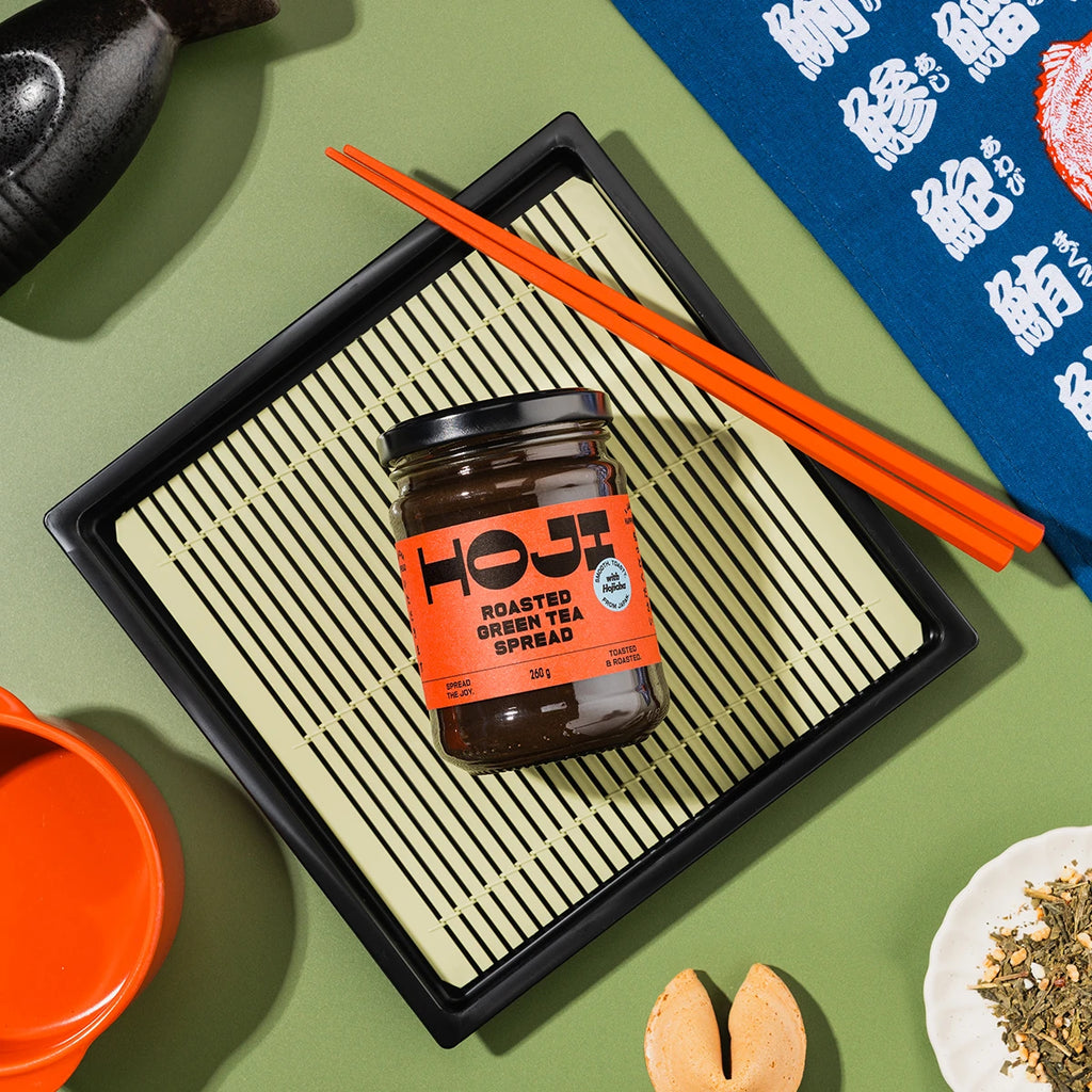 Jar of HOJI Roasted Green Tea Spread on a black tray with orange chopsticks on a green surface.