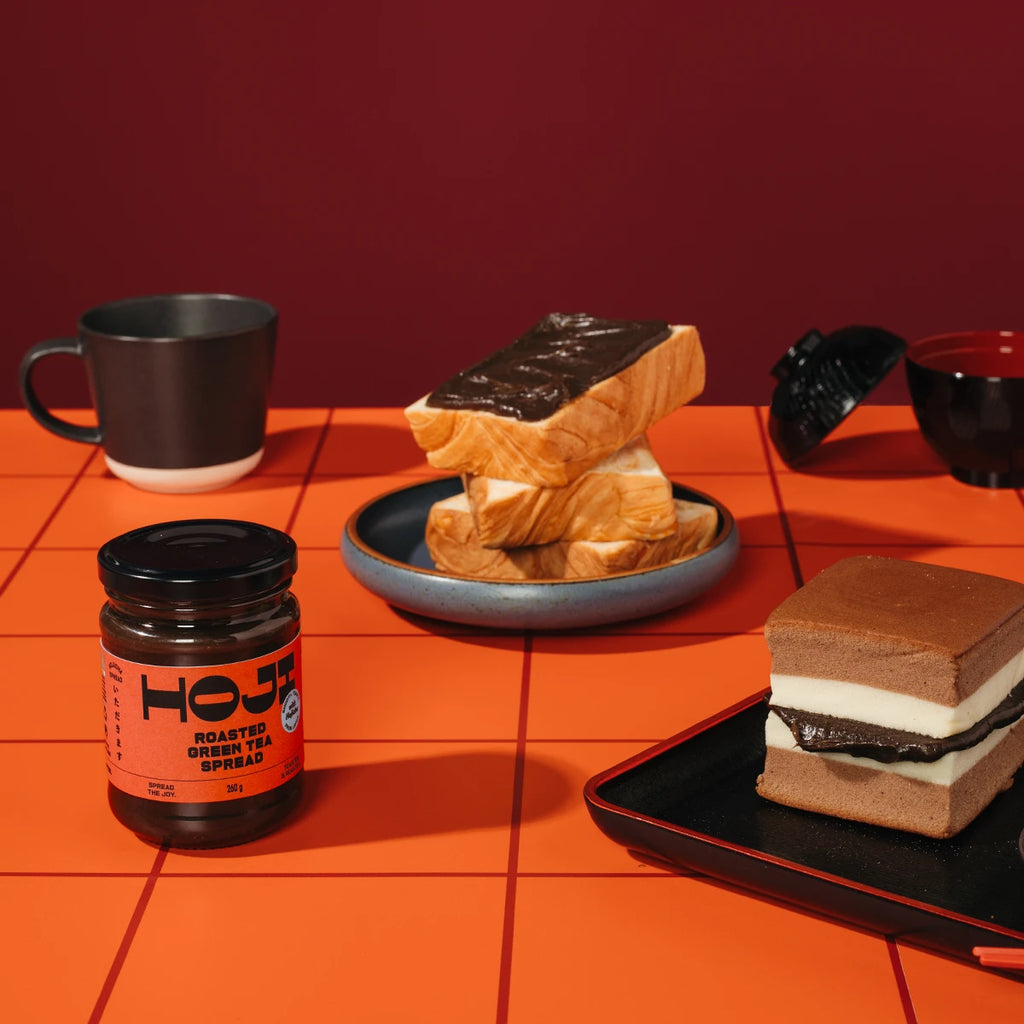 Jar of HOJI roasted green tea spread with toasts and a cake on an orange surface