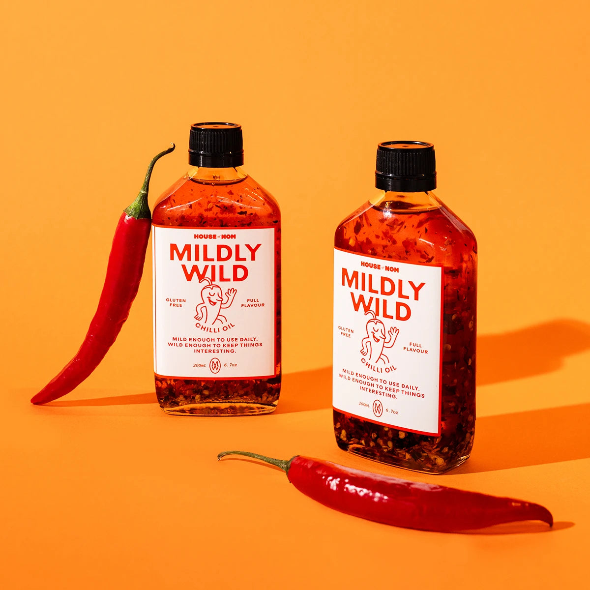 Two bottles of 'Mildly Wild' chilli oil with red peppers on an orange background