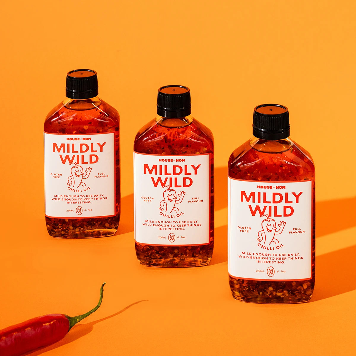 Three bottles of 'Mildly Wild' chili oil on an orange background with a red chili pepper.