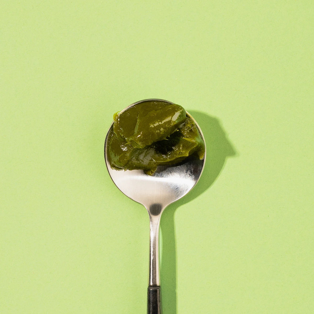 Spoon with MOJI matcha green tea spread  on a light green background
