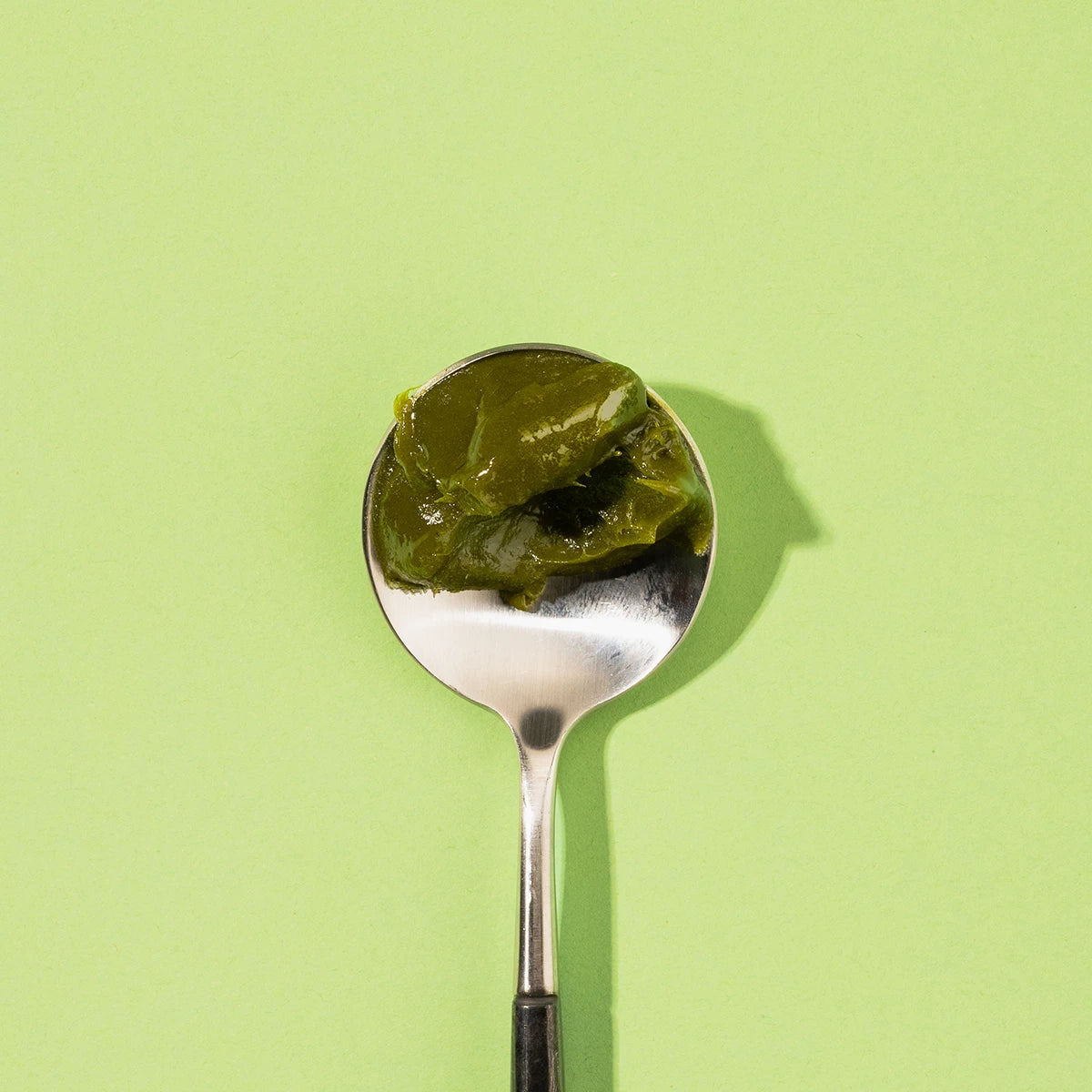 Spoon with MOJI matcha green tea spread  on a light green background